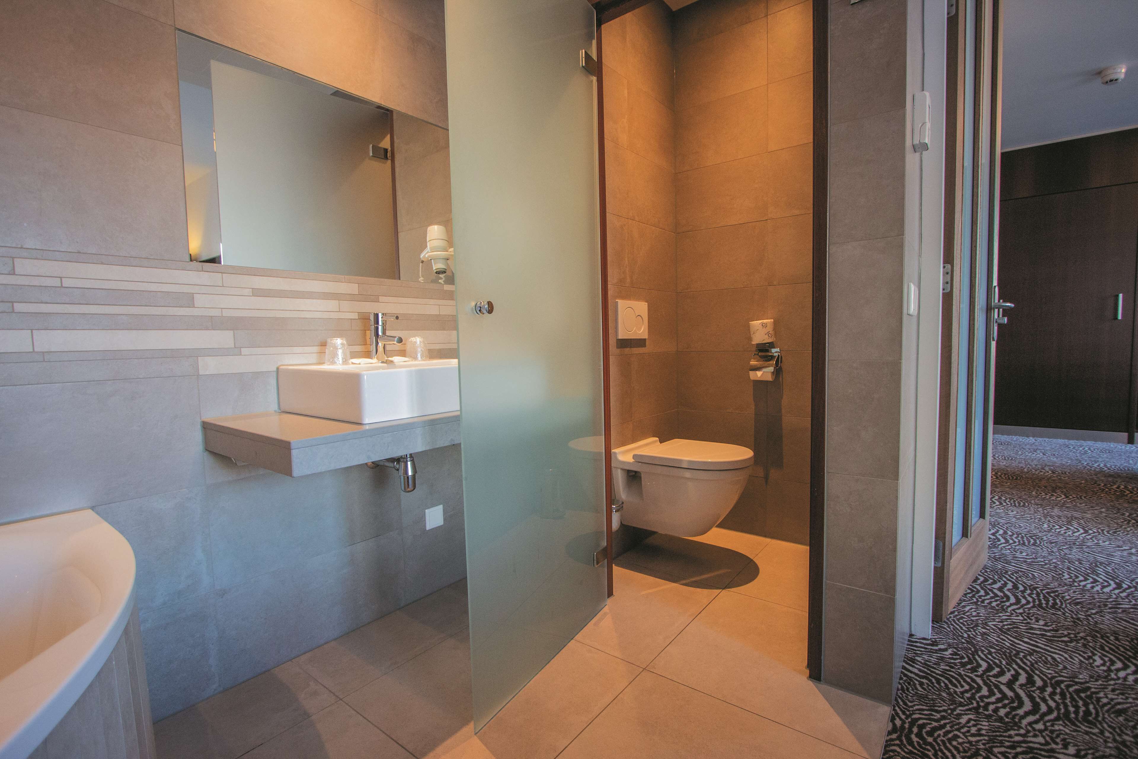 Un bany modern amb plat de dutxa envoltat de vidre, un lavabo blanc i un vàter.