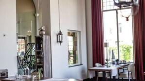 A dining area with a long table, chairs, and a wine rack. There is a window with curtains and a view of greenery outside. - Golden Tulip West Ende (Helmond)