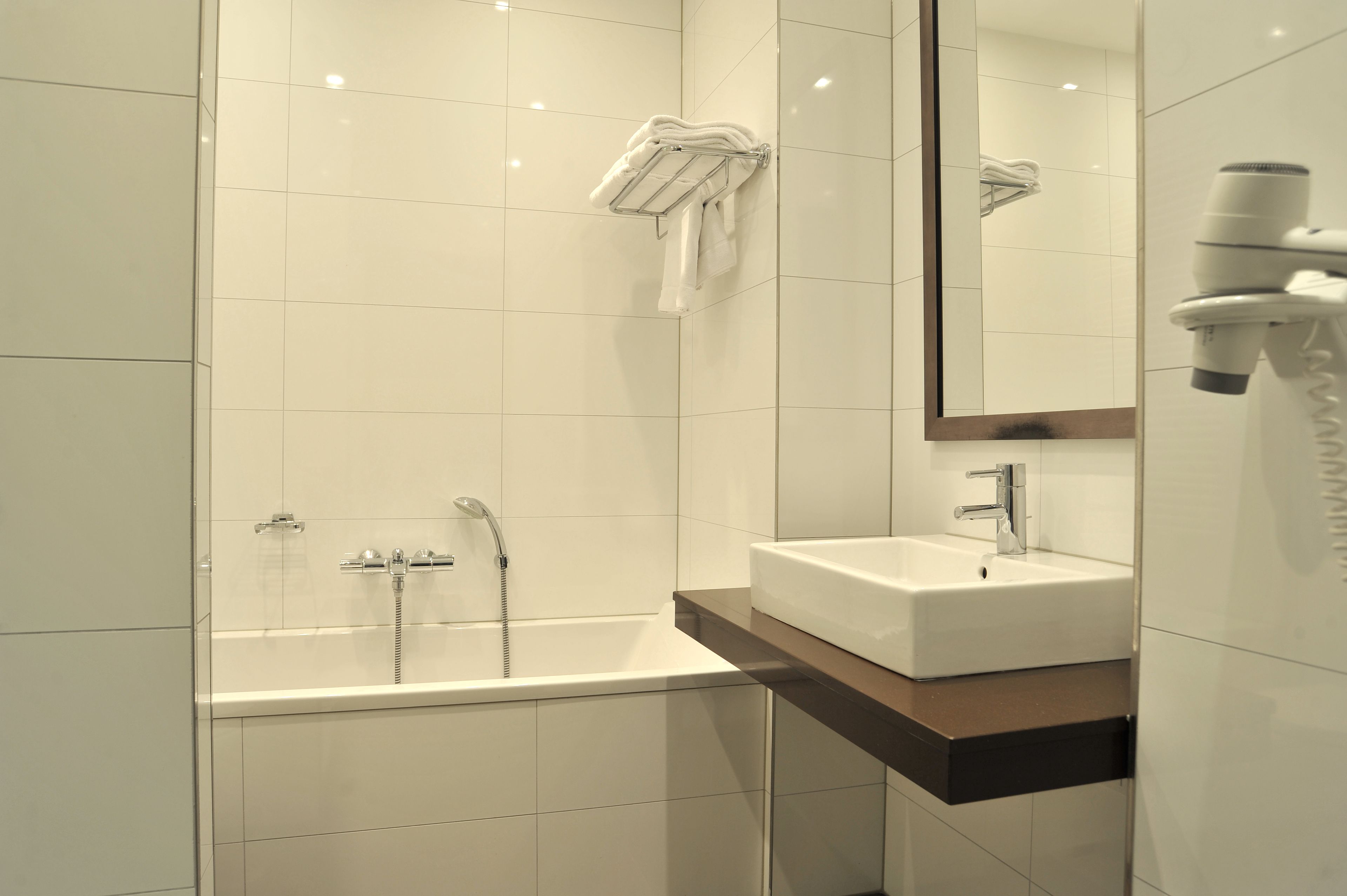 Een moderne badkamer met een badkuip, wastafel en een aan de muur bevestigde haardroger.