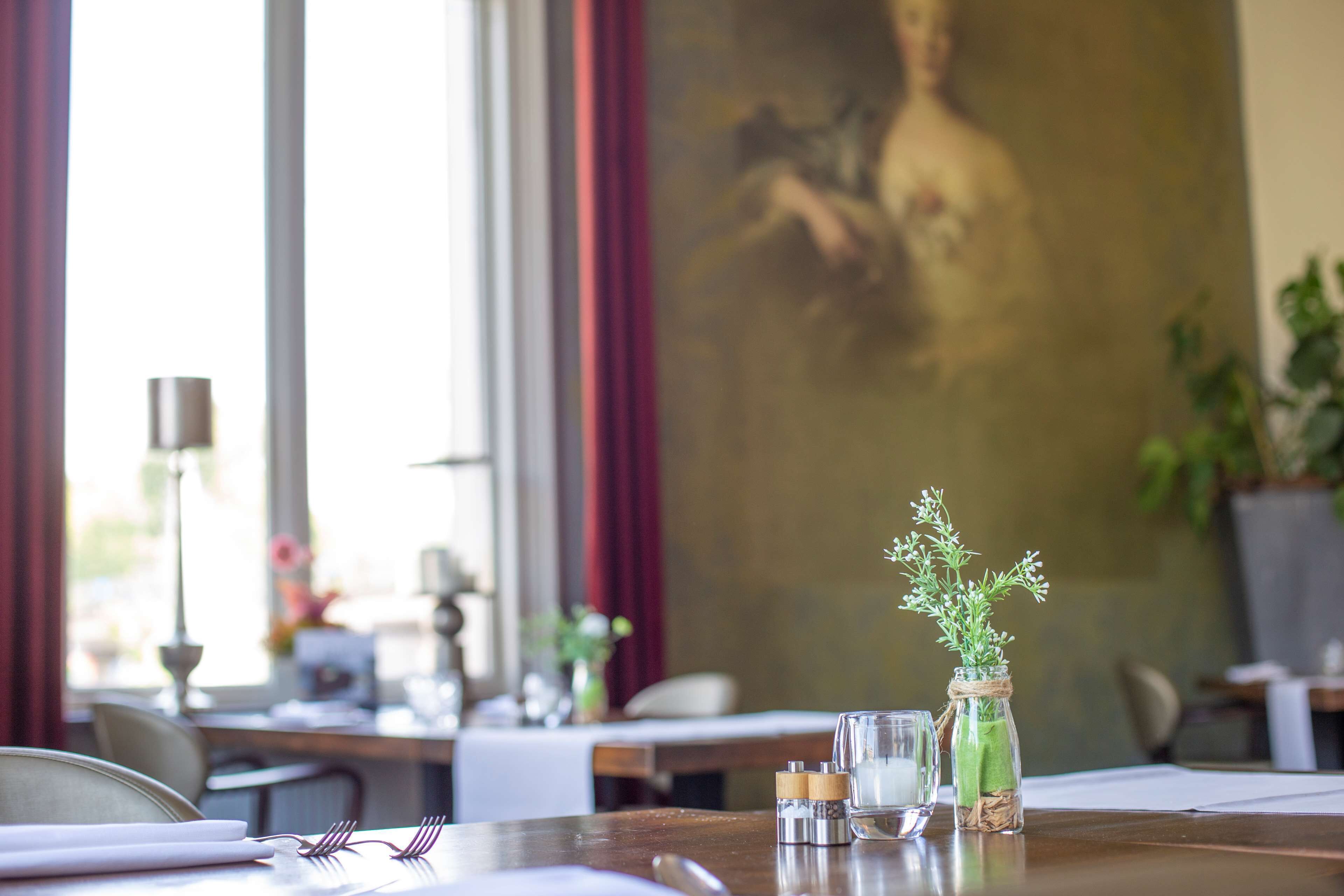 A dining table with a glass bottle of herbs, a salt shaker, and a candle. There is a painting on the wall behind the table.