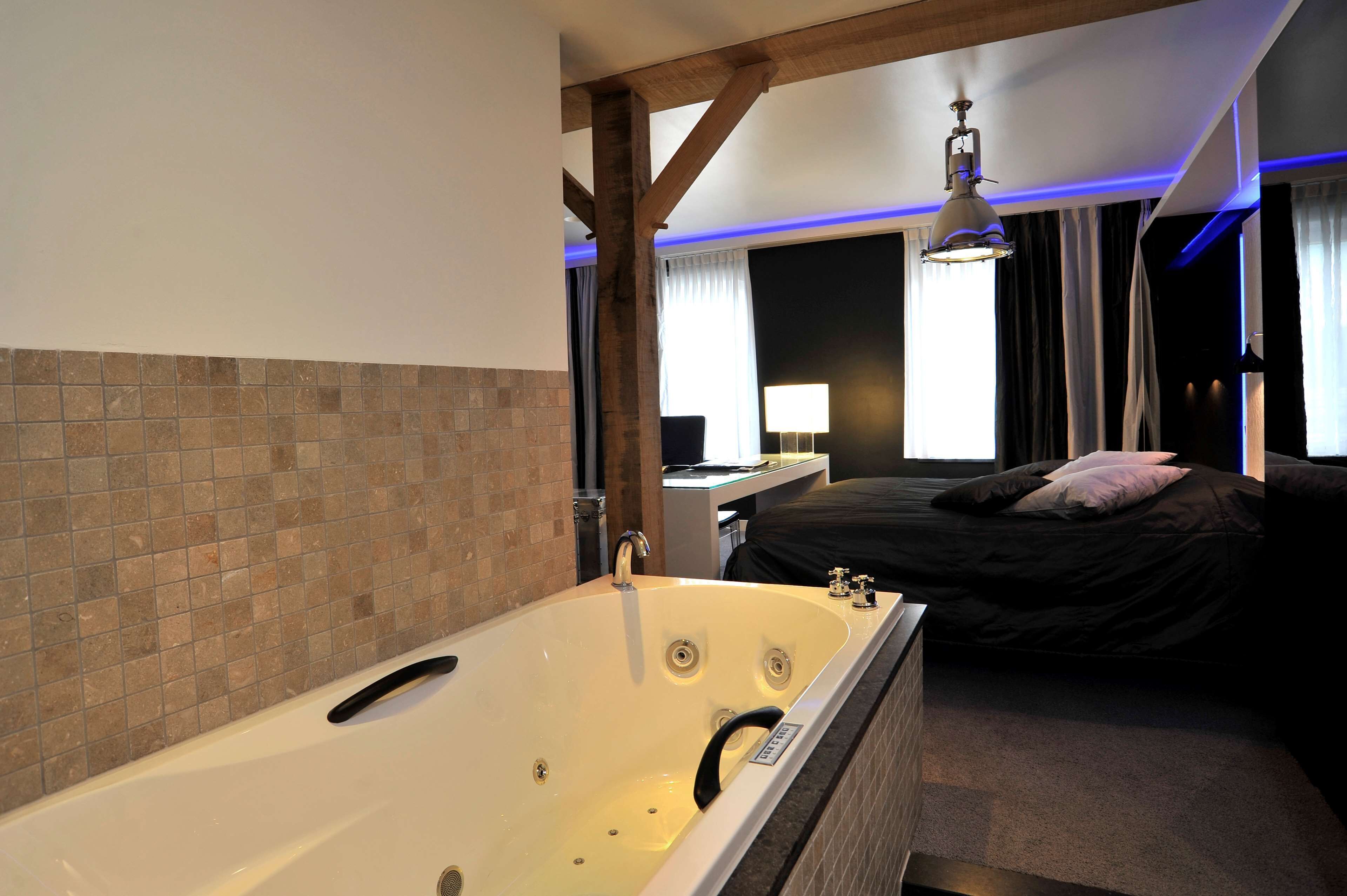 A modern bedroom with a large bathtub, a bed, a desk, and a window with curtains.