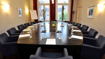 Un salón de conferencias con una gran mesa ovalada, sillas negras y una pizarra.