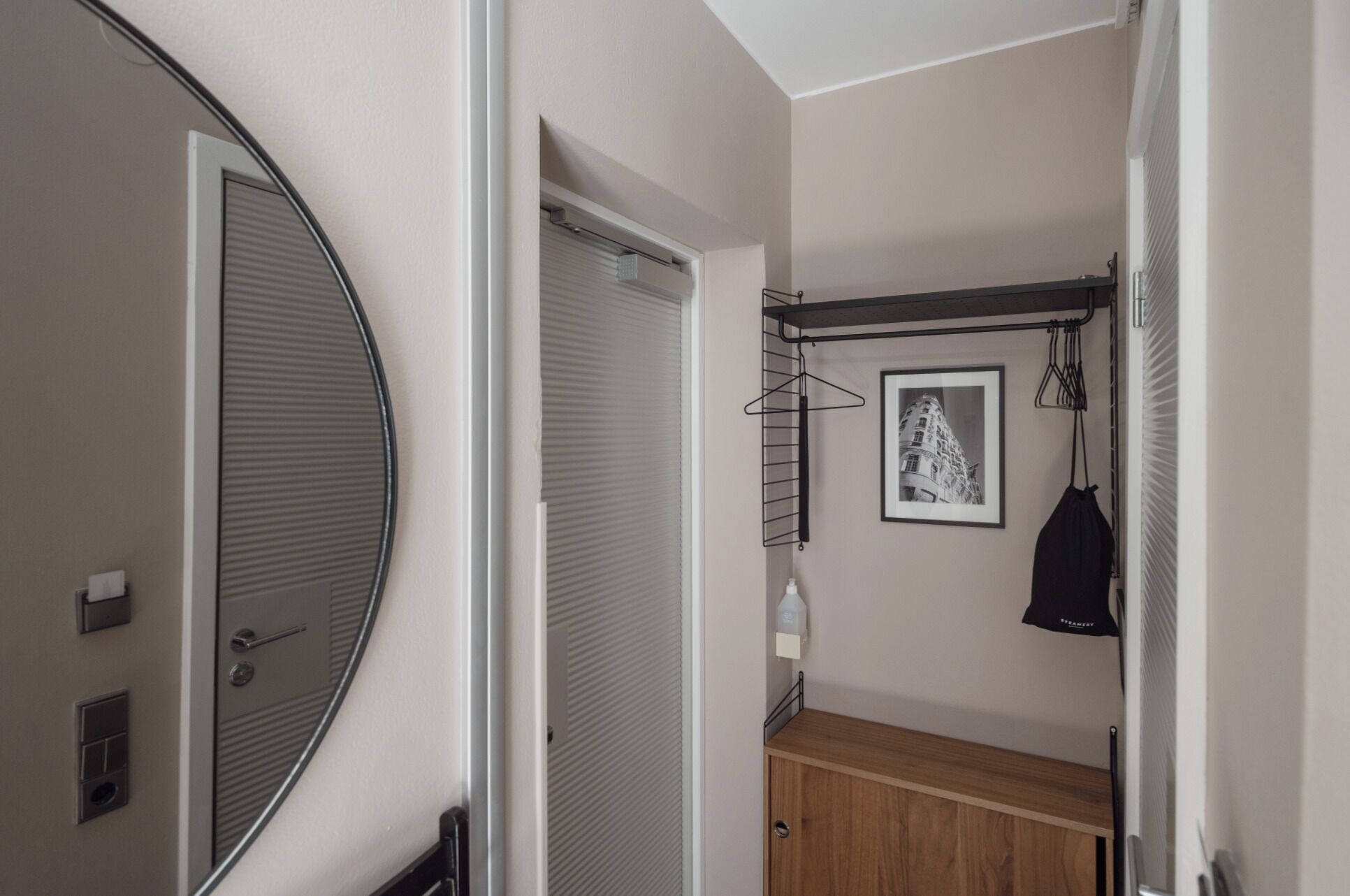 Un couloir étroit avec une armoire en bois, un manteau noir suspendu à un porte-manteau et un tableau encadré accroché au mur.