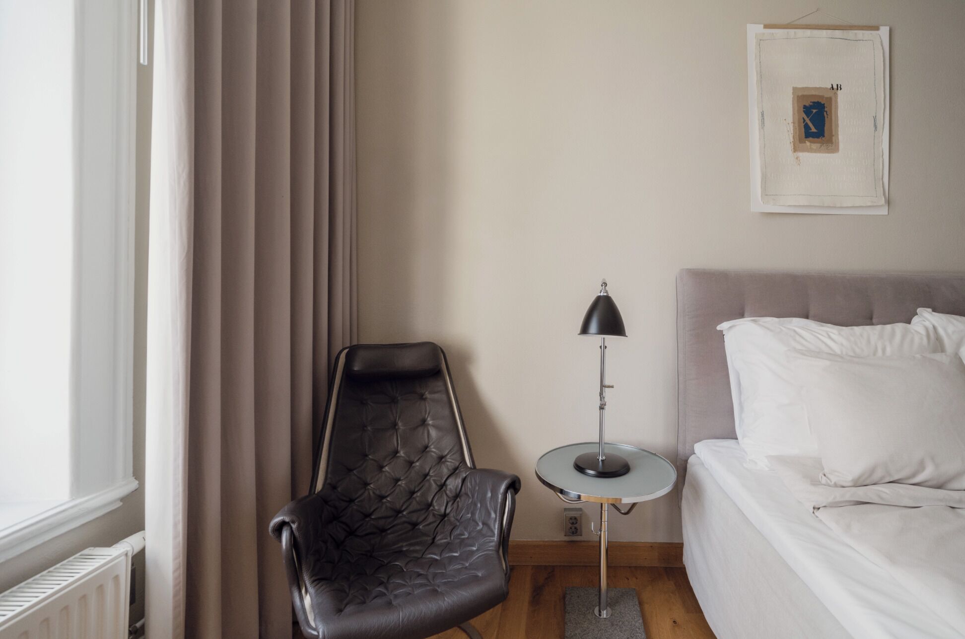 Et hotelværelse med seng, stol, lampe og et vindue med gardiner.
