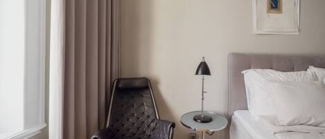 A hotel room with a bed, a chair, a lamp, and a window with curtains.