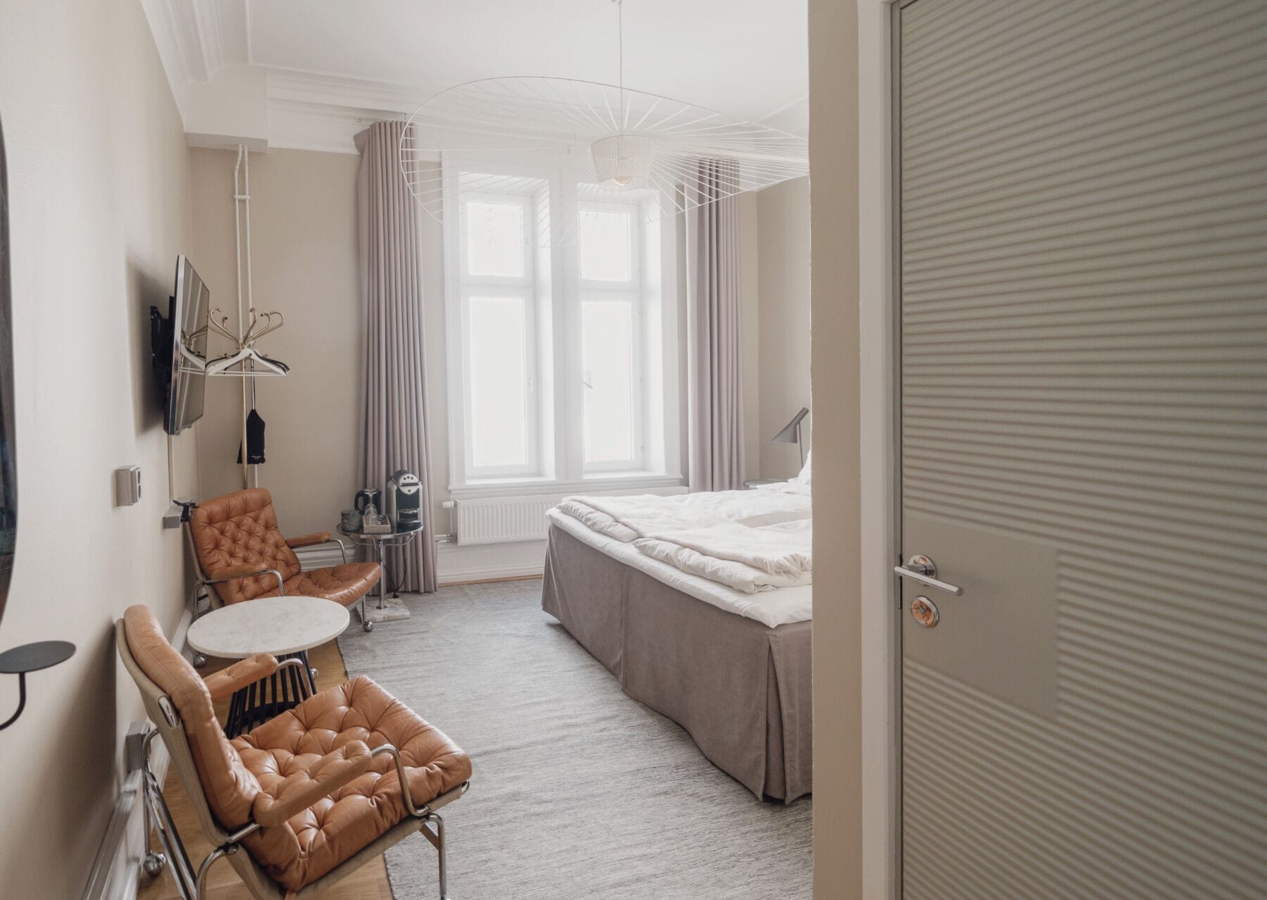 Ein Hotelzimmer mit Bett, einer Sitzecke mit Tisch und Stühlen, einem Fernseher und einem fenster mit Vorhängen.