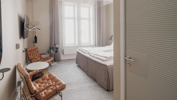 Une chambre d’hôtel comprenant un lit, un coin salon avec une table et des chaises, un téléviseur et une fenêtre avec des rideaux.