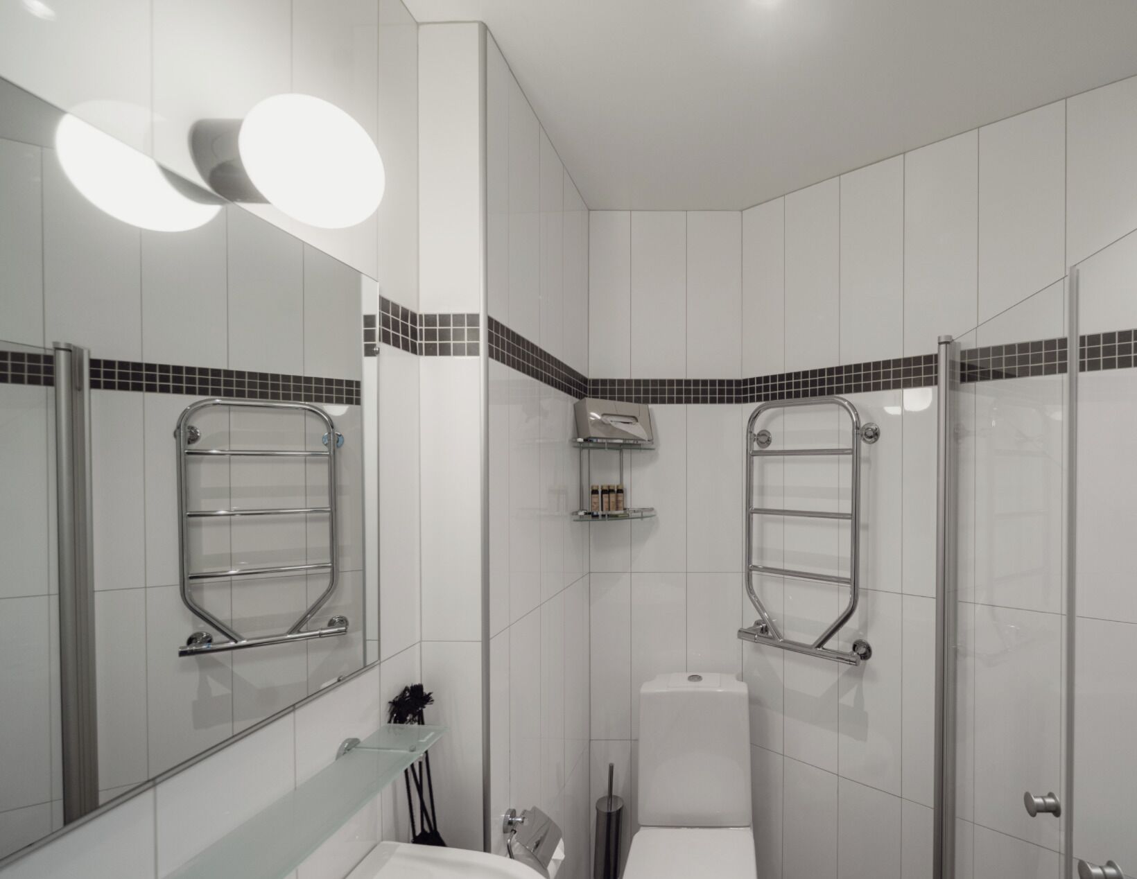 A modern bathroom with white tiles, a glass shower enclosure, and a toilet.