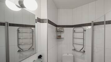 A modern bathroom with white tiles, a glass shower enclosure, and a toilet.