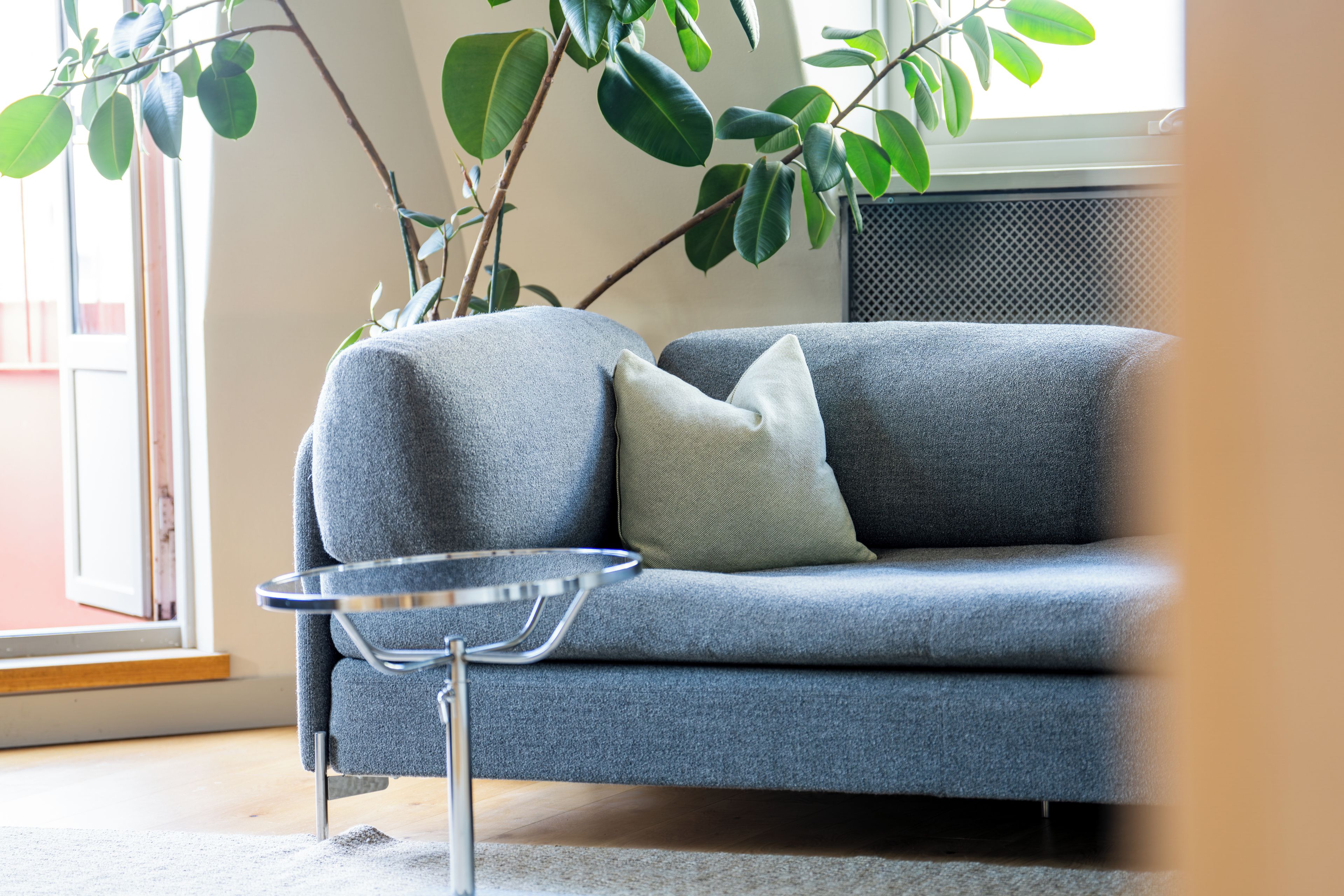 En grå soffa med en kudde, ett litet metallbord och en växt i bakgrunden.