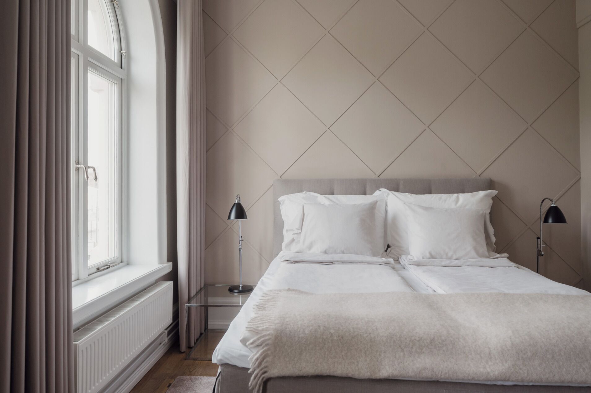 A neatly made bed with white linens, a grey headboard, and two bedside lamps.