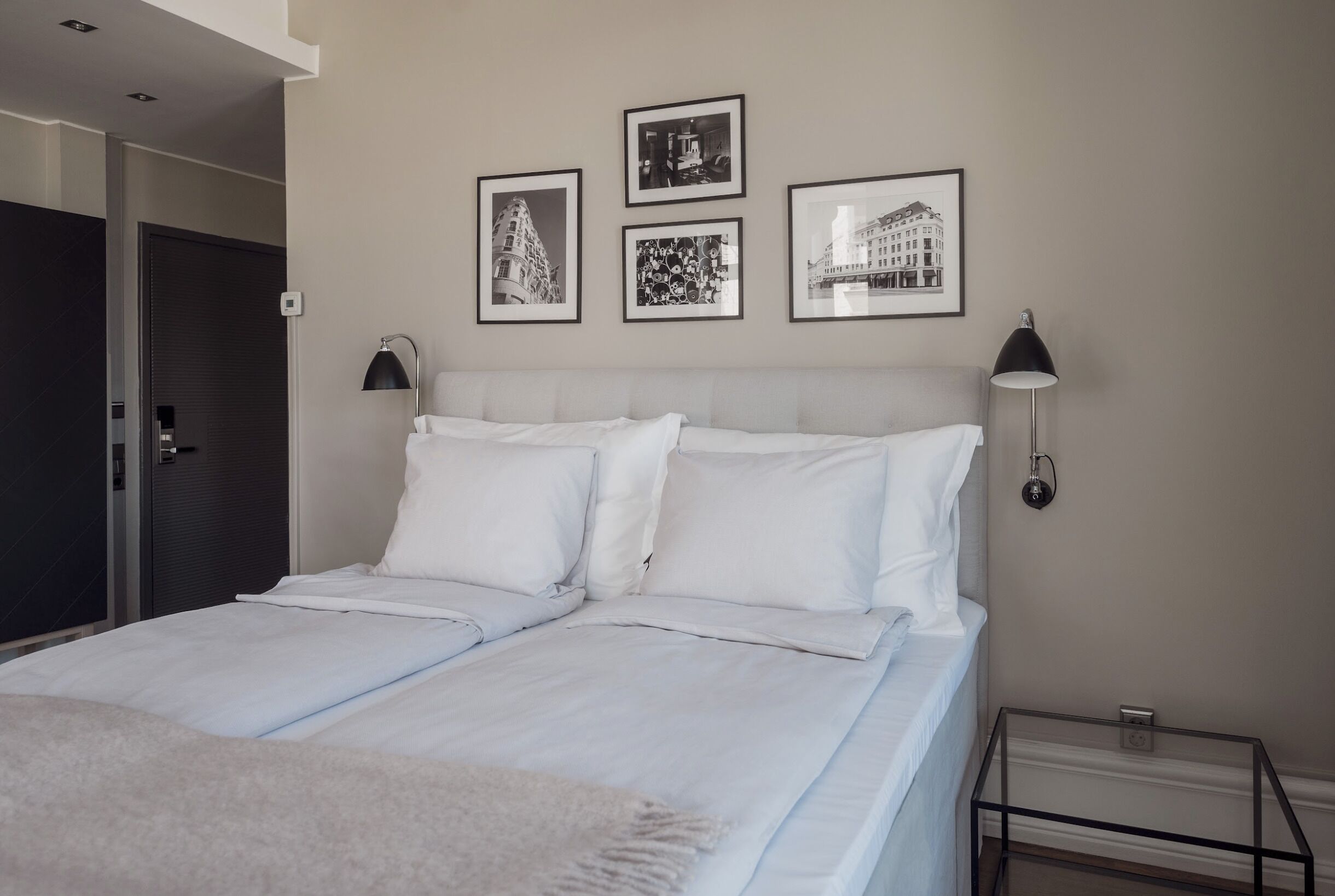 A neatly made double bed with white linens, two bedside lamps, and three framed pictures on the wall.