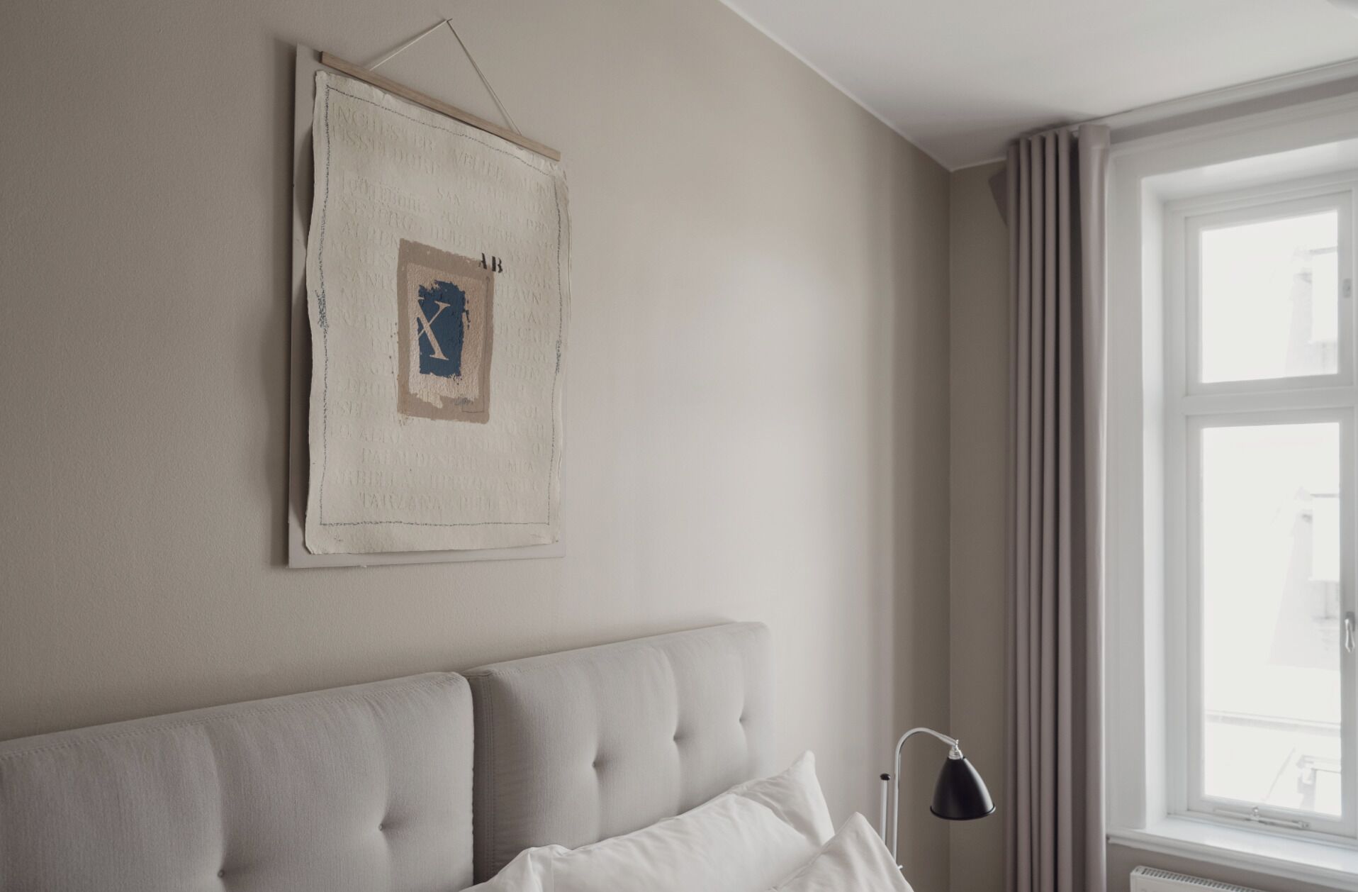 Une chambre à coucher avec un lit, une œuvre d’art suspendue au mur et une fenêtre avec des rideaux.