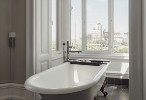A bathroom with a freestanding bathtub, a window with a view of buildings, and a towel rack. - TwentySix (Malmö)
