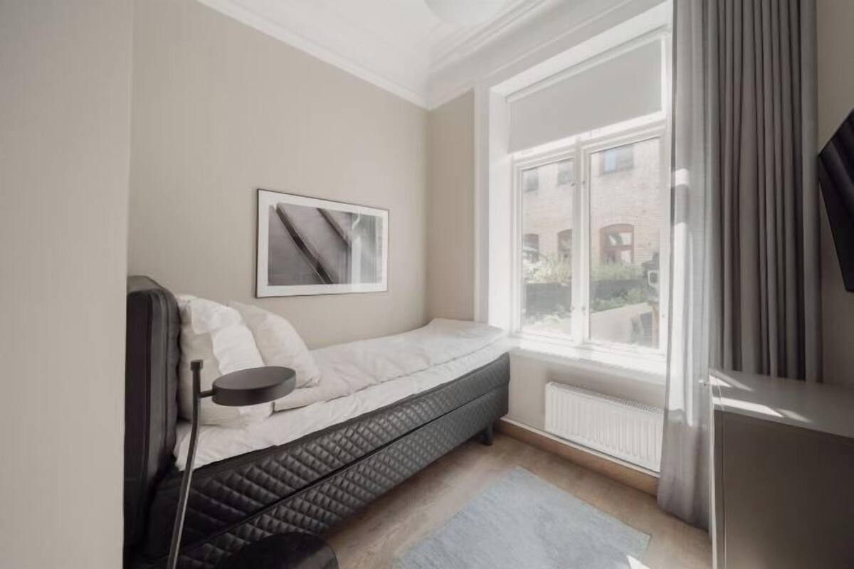 A bedroom with a bed, a window, a radiator, and a picture on the wall.