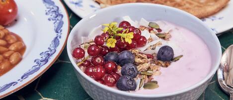A breakfast table with plates of pancakes, berries, and a bowl of yogurt with fruits.