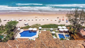A beach resort with a swimming pool, beach umbrellas, and a view of the ocean. - Le Relais La Borie (Búzios)