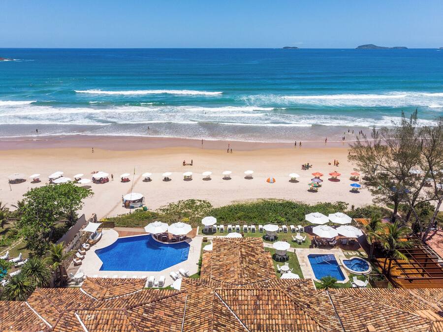 A beach resort with a swimming pool, beach umbrellas, and a view of the ocean.