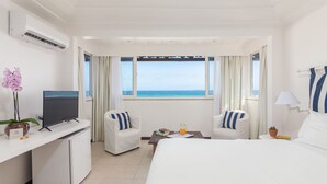 A hotel room with a bed, two chairs, a desk with a TV, a small table with a drink, and a view of the sea. - Le Relais La Borie (Búzios)
