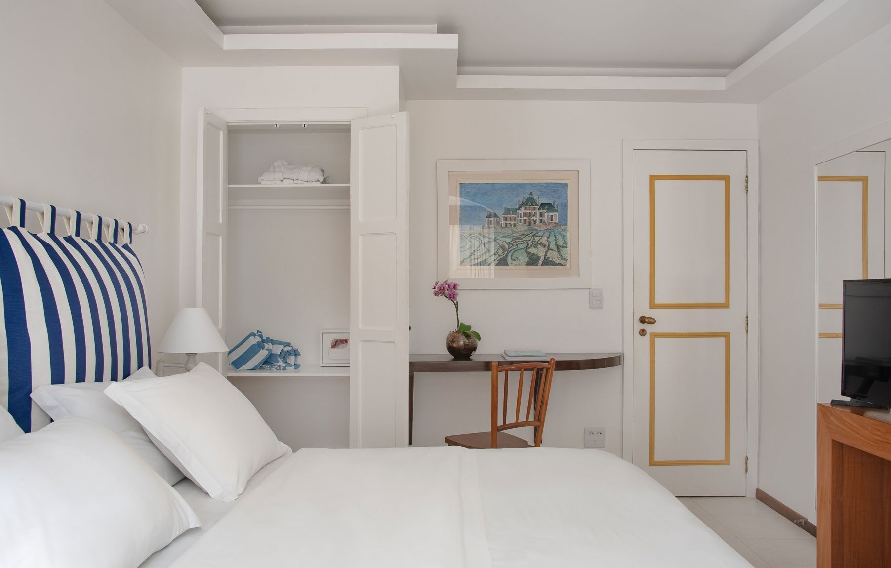 A hotel room with a bed, a desk, a chair, a TV, and a wardrobe.
