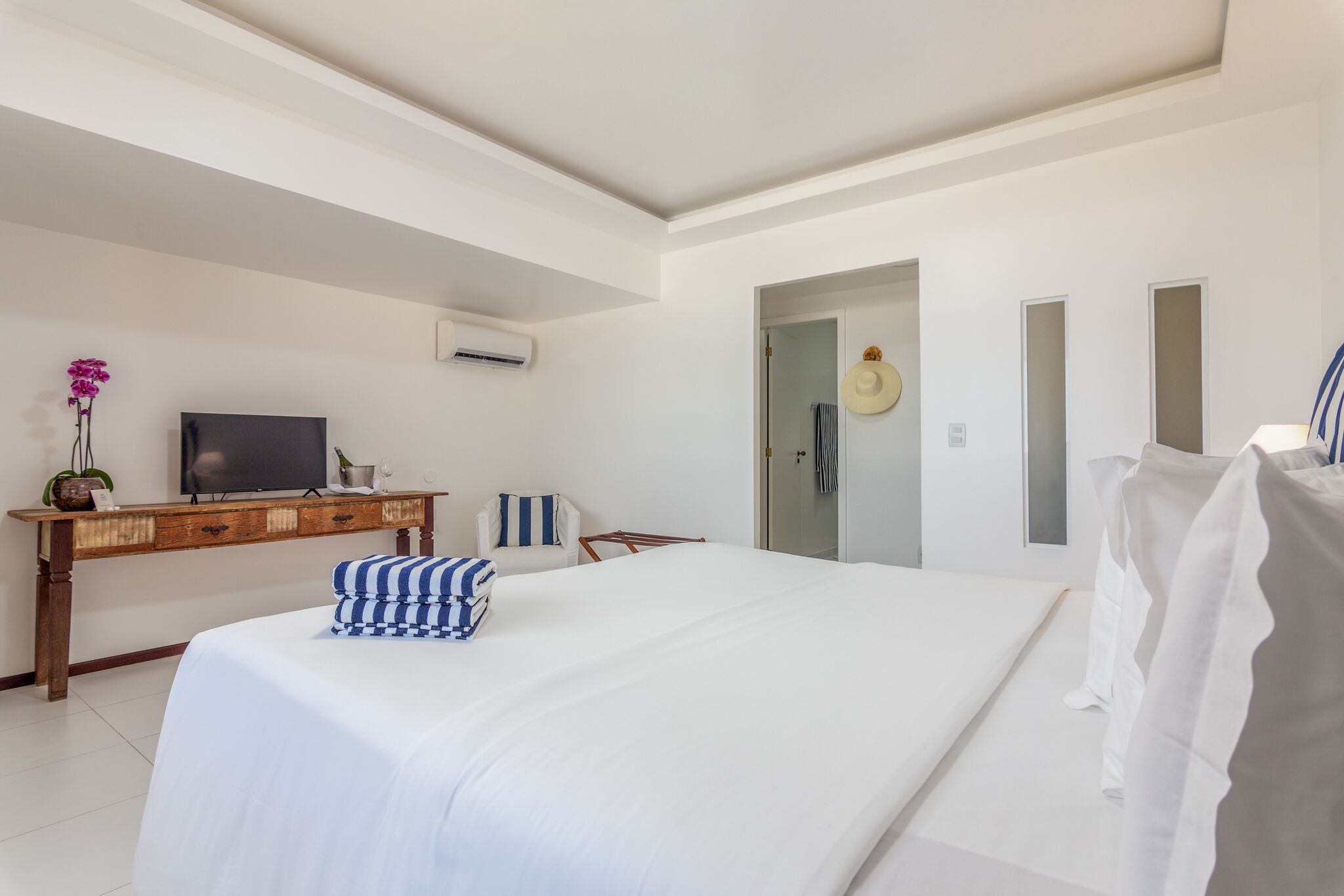Habitación de hotel con una cama grande, un escritorio de madera con un televisor, una planta pequeña y una puerta que da a un baño.