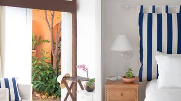 Habitación de hotel con cama, mesita de noche con lámpara, una silla y vista a un jardín por la ventana.