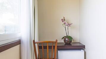 A corner room with a wooden chair, a small white refrigerator, and a vase with flowers on a counter.