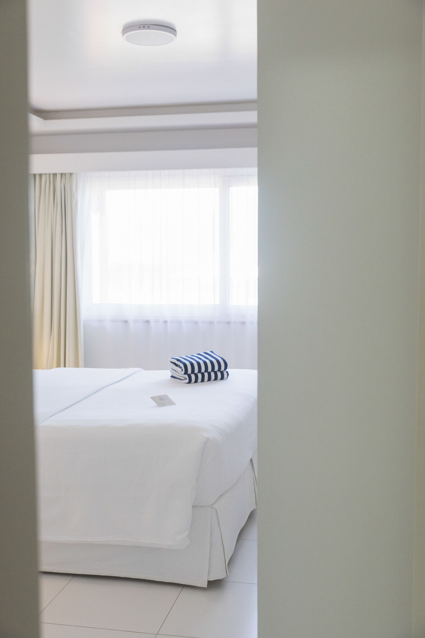 A hotel room with a bed, a window with curtains, and a white ceiling.