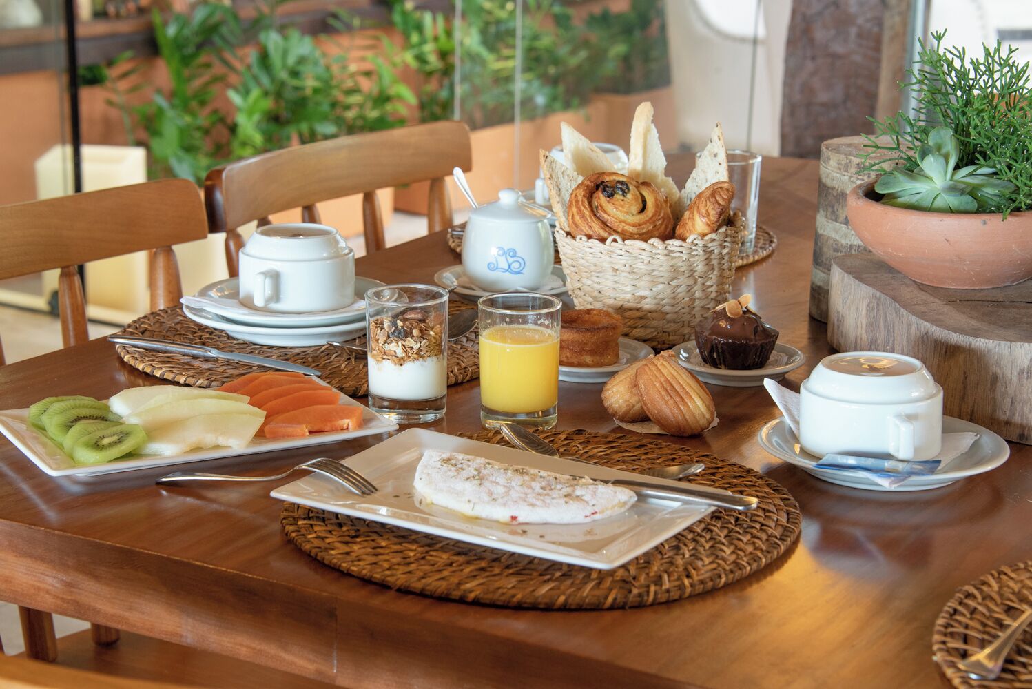 Un desayuno con platos de fruta, pastelería y bebidas sobre una mesa de madera.