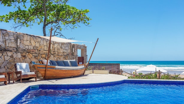 A swimming pool with a wooden boat, lounge chairs, and a stone wall. - Le Relais La Borie (Búzios)