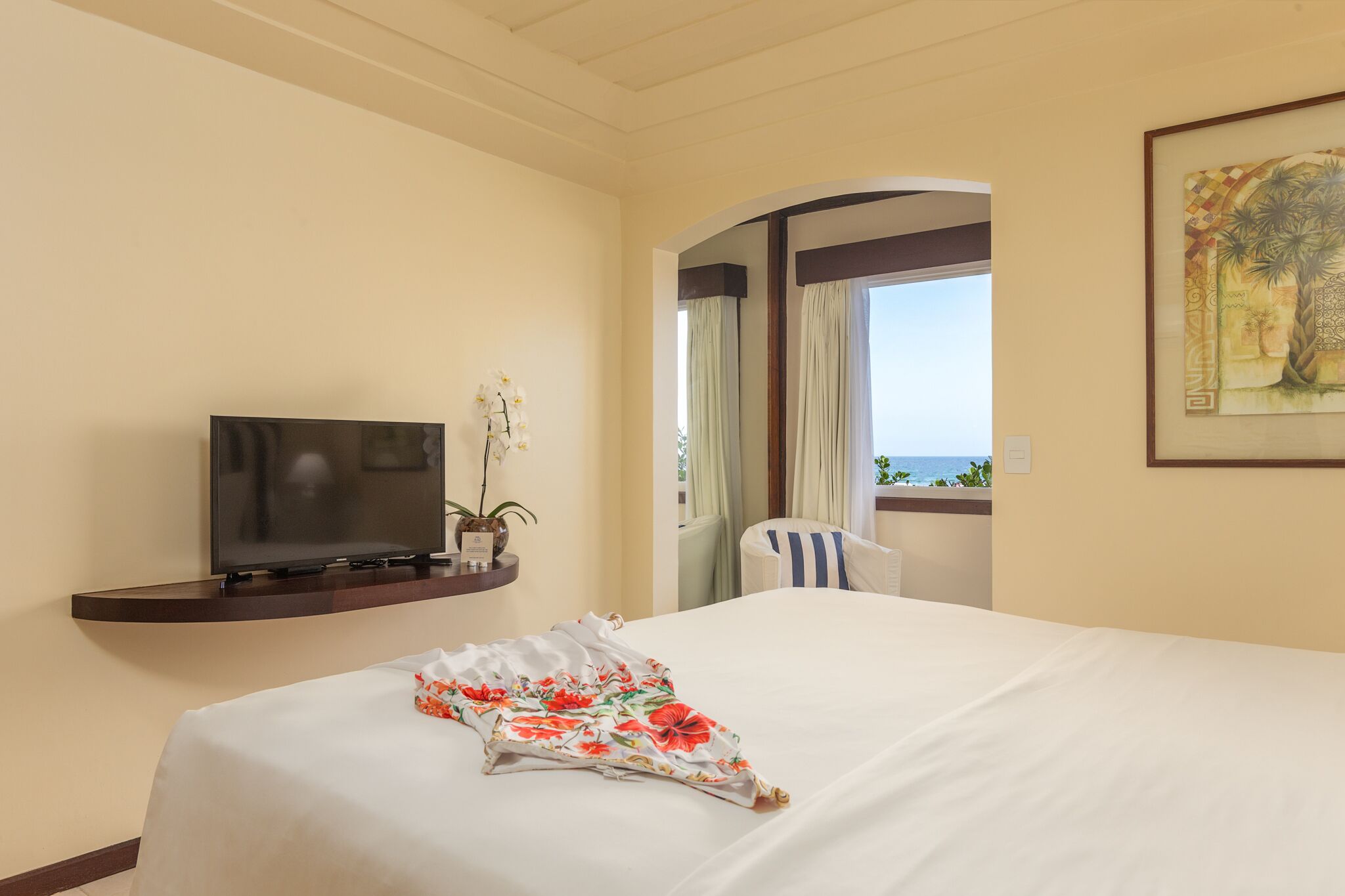 A hotel room with a bed, a TV on a shelf, a chair, and a window with curtains.
