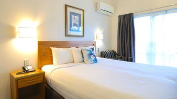 Quarto de hotel com uma cama, abajures, um telefone, um quadro emoldurado, ar condicionado e uma janela com cortinas.