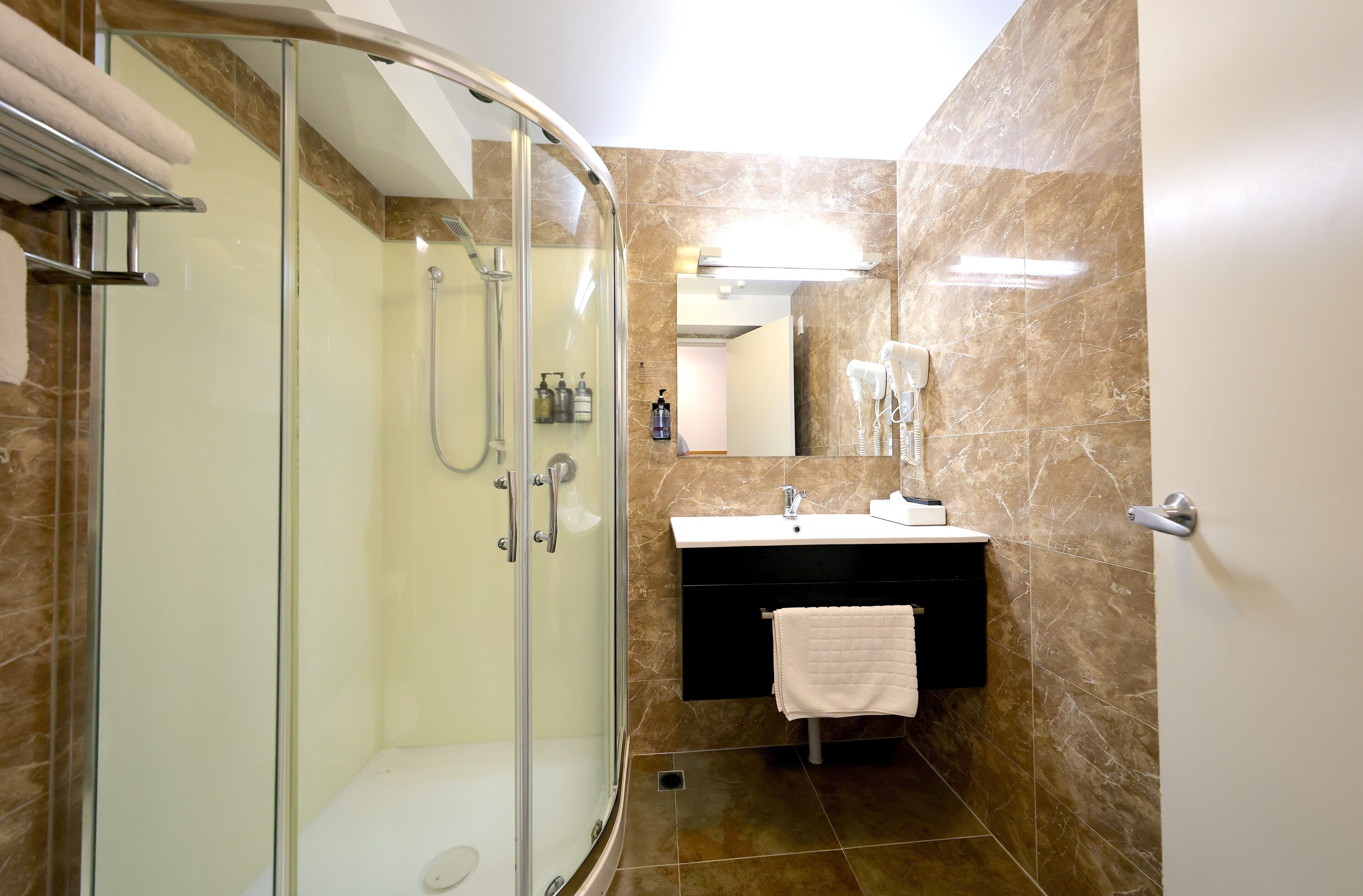 A modern bathroom with a glass-enclosed shower, a white sink, and a marble-tiled wall.