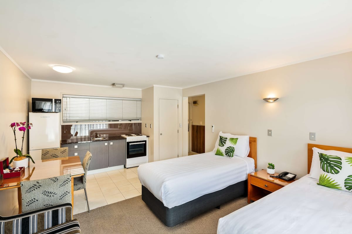 A hotel room with two beds, a kitchenette, a dining area, and a bathroom.