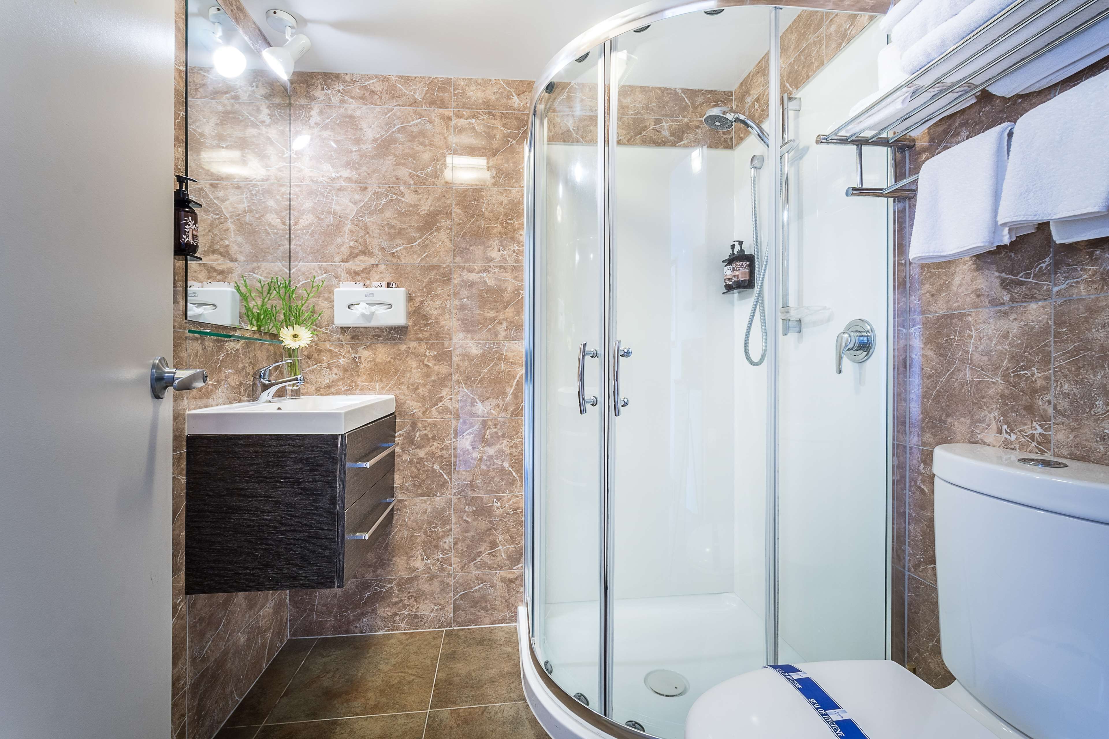 Et moderne badeværelse med en glasafskærmet brusekabine, toilet og vaskebord med spejl og vask.
