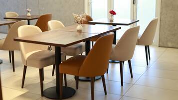 A modern dining area with tables and chairs, a vase with flowers, and a view through a glass door.