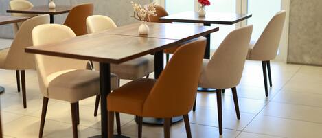 A modern dining area with tables and chairs, a vase with flowers, and a view through a glass door.