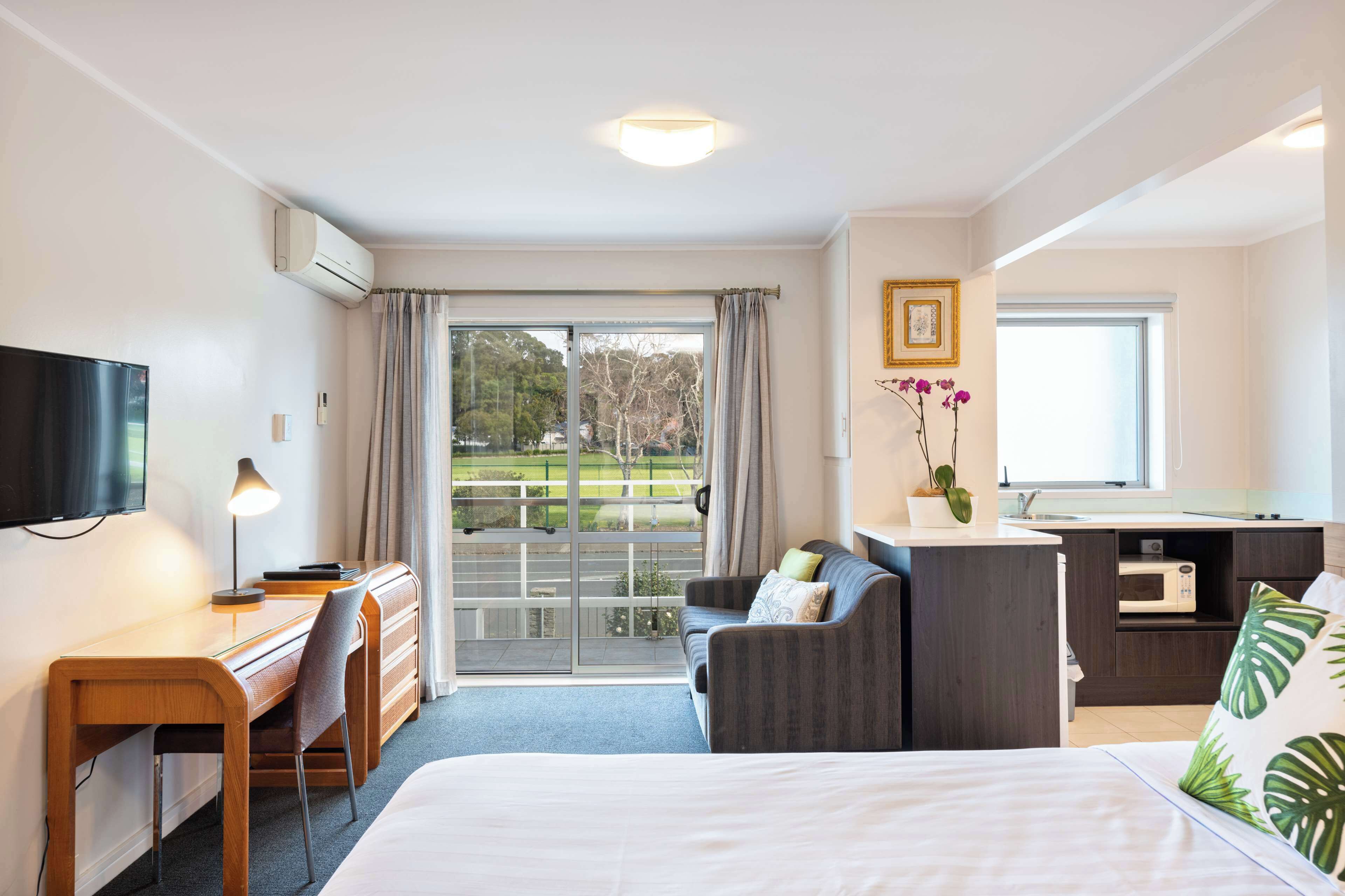 A hotel room with a bed, desk, chair, and a kitchenette.