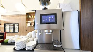 Une machine à café dotée d’un écran numérique, un réfrigérateur et une pile d’assiettes blanches sur un comptoir.