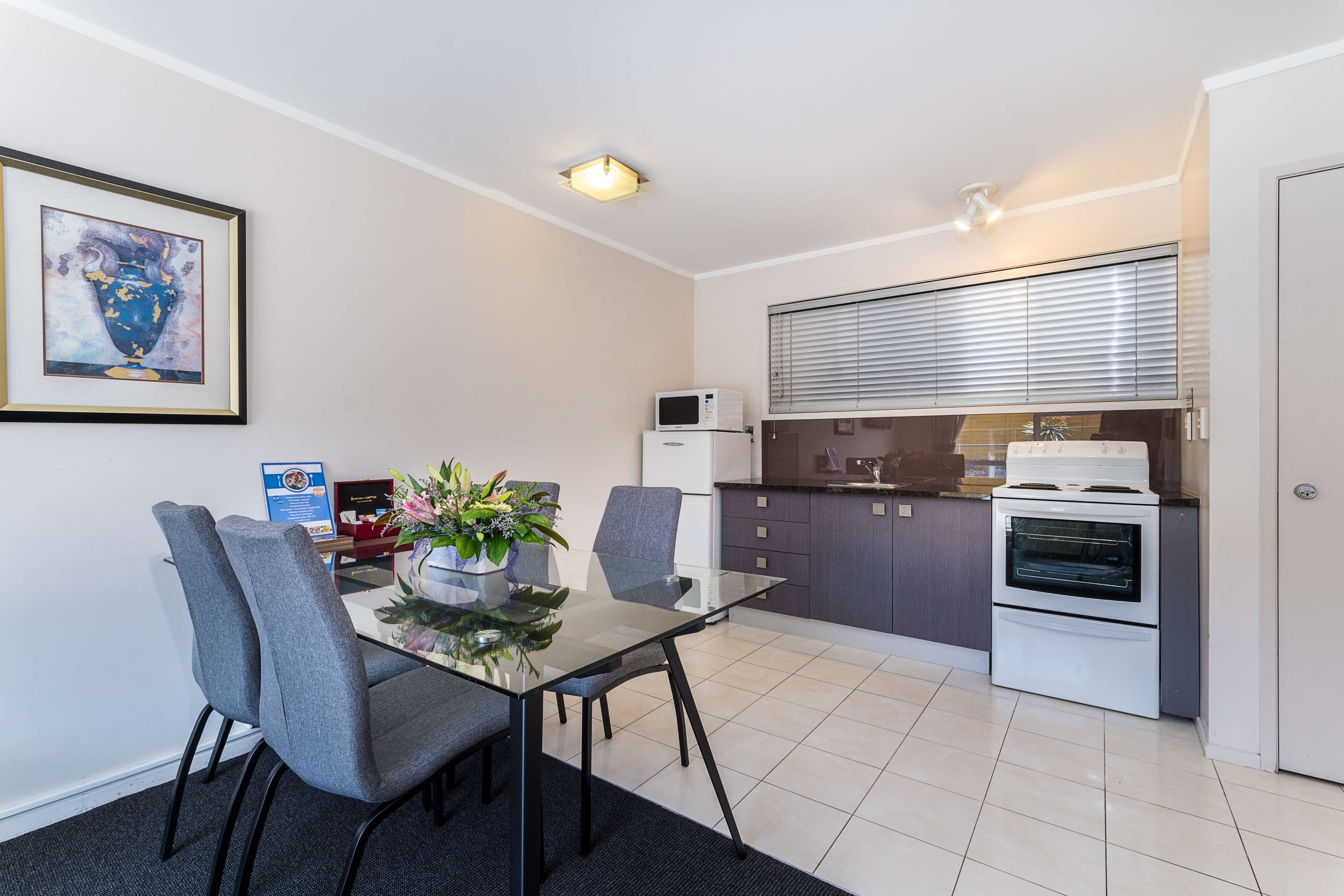 A modern kitchen with a microwave, oven, and a dining area with a glass table and grey chairs.