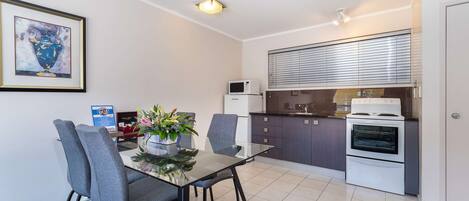A modern kitchen with a microwave, oven, and a dining area with a glass table and grey chairs.