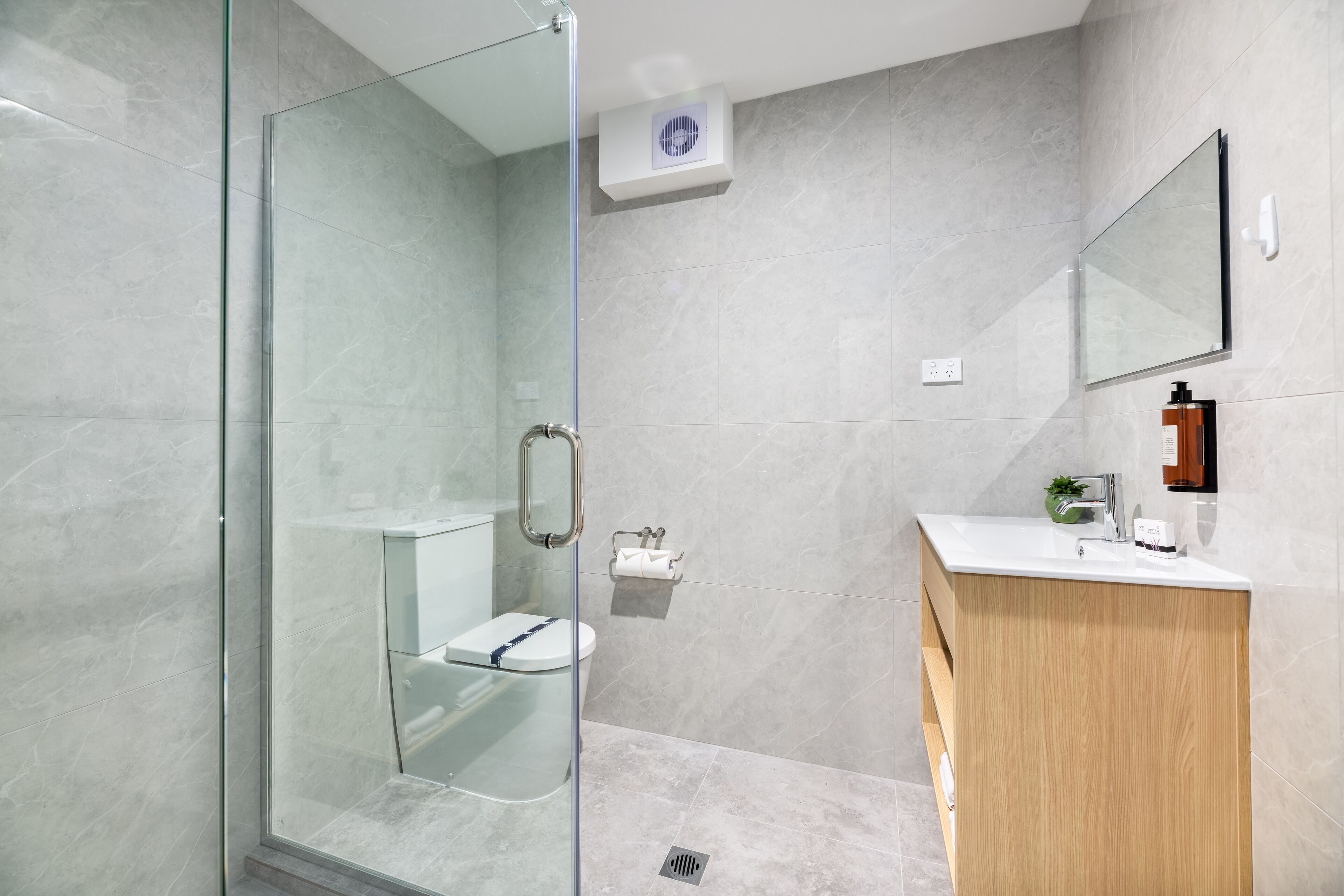 Un bagno moderno con cabina doccia in vetro, un WC, un lavabo con specchio e un mobile vanitario in legno.