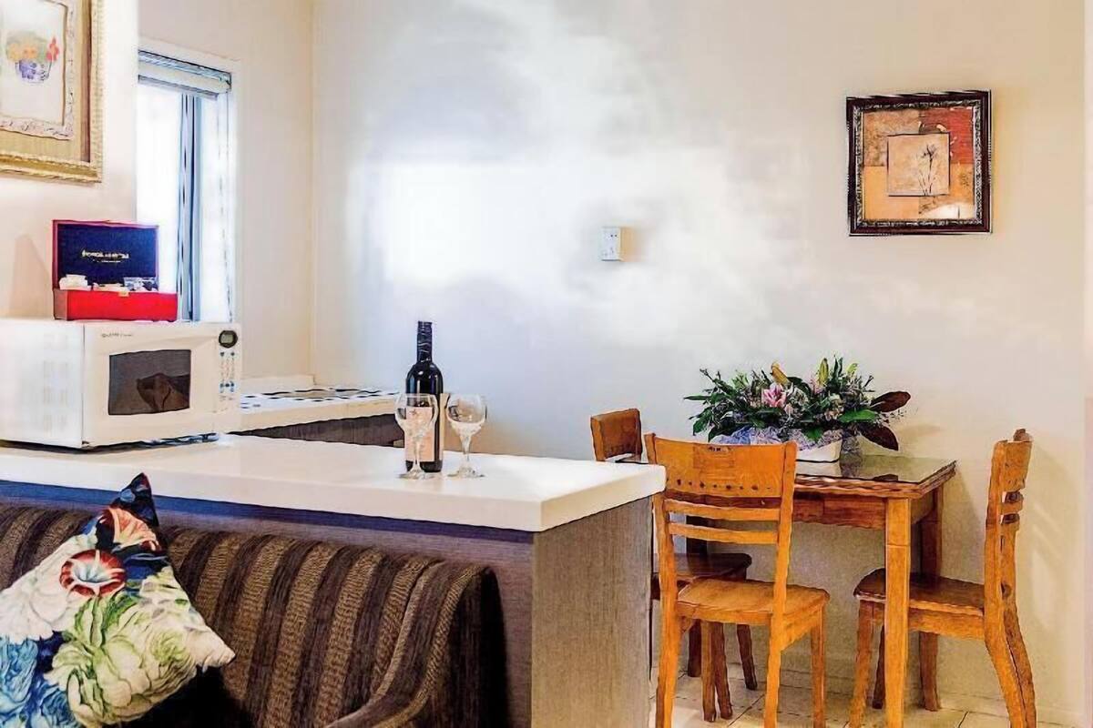 A kitchen with a microwave, a wine bottle, and glasses on the counter. There is a dining table with chairs and a potted plant.