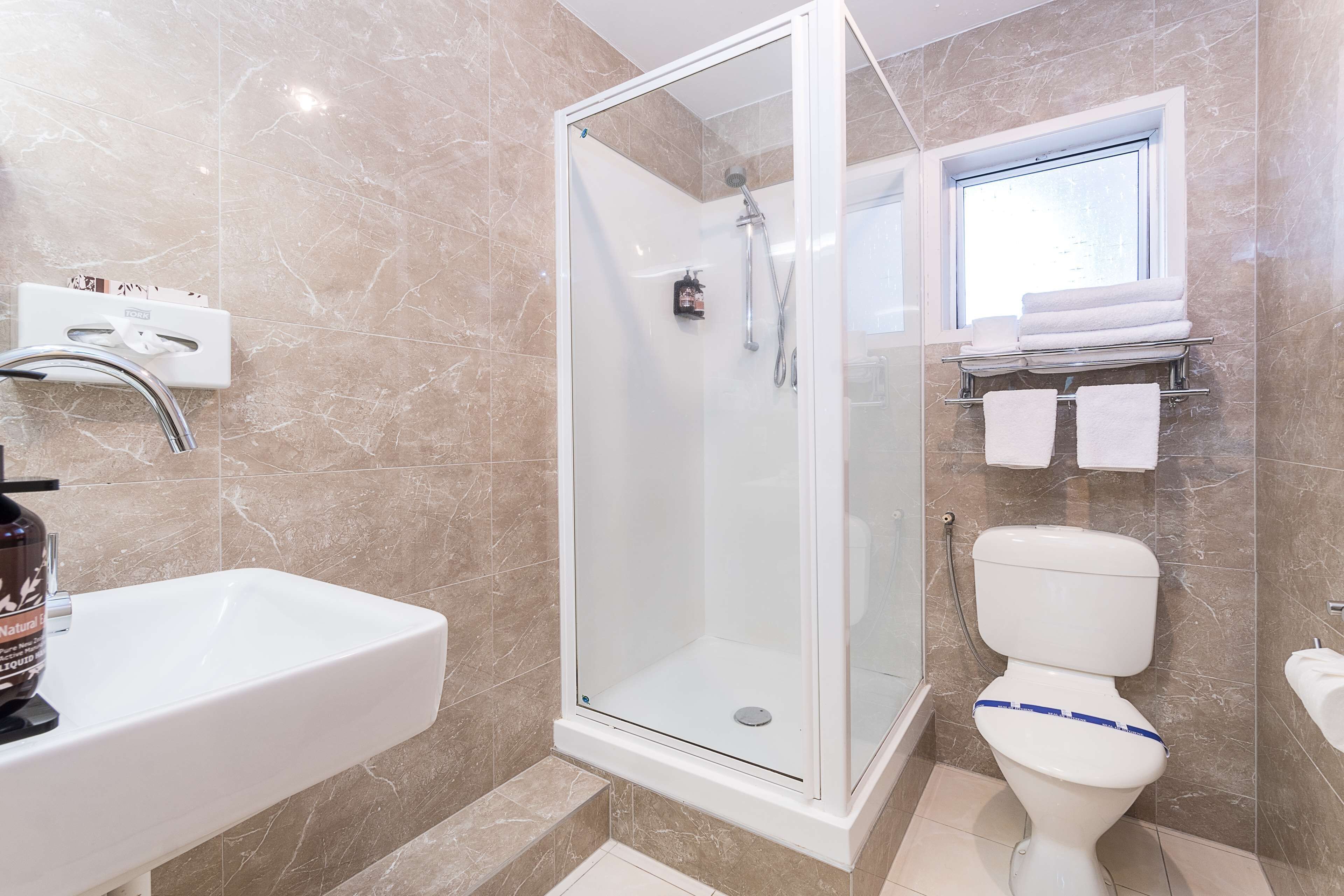 A bathroom with a glass-enclosed shower, a white sink, and a toilet with a blue stripe.