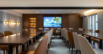 A conference room with a long table, chairs, a TV screen, and a shelf with decorative items.