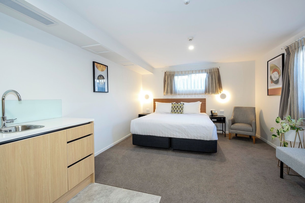 A hotel room with a bed, bedside table, chair, and a small desk with a telephone.