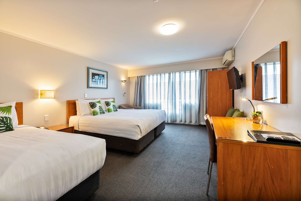 A hotel room with two beds, a desk, a chair, a TV, and a window with curtains.