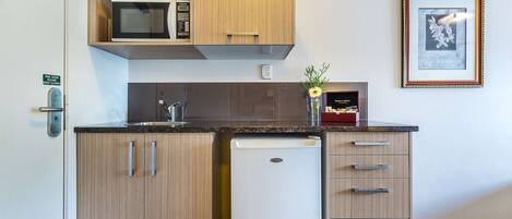 Una cocina compacta con armarios de madera, microondas, lavavajillas y un cuadro en la pared.