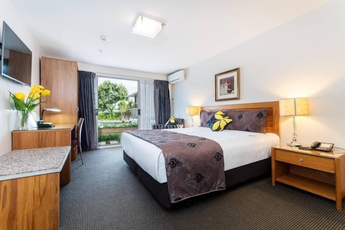 A hotel room with a bed, bedside table, lamp, desk, chair, and a window with curtains.