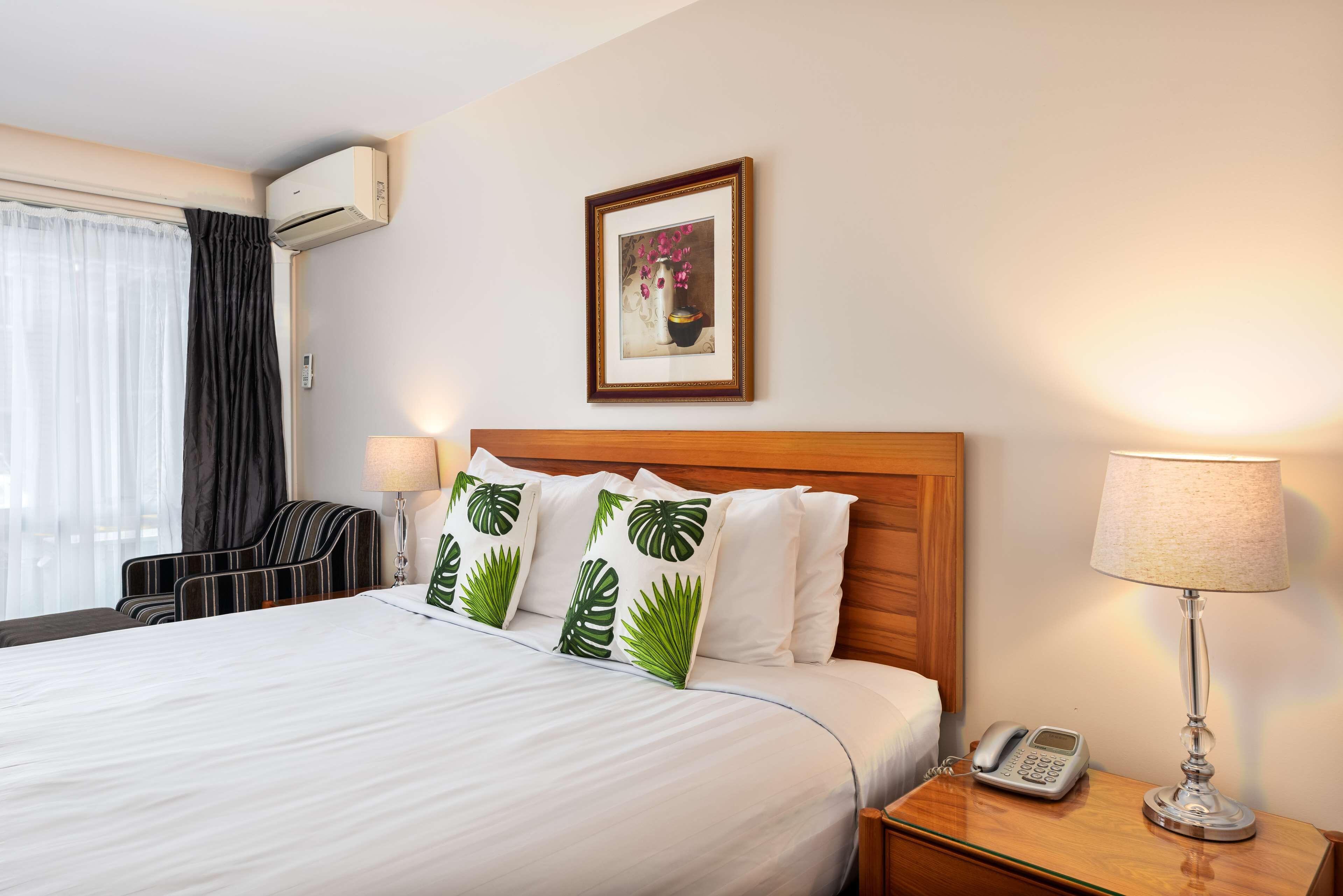 A hotel room with a large bed, a bedside table with a lamp, a phone, and a framed picture on the wall.